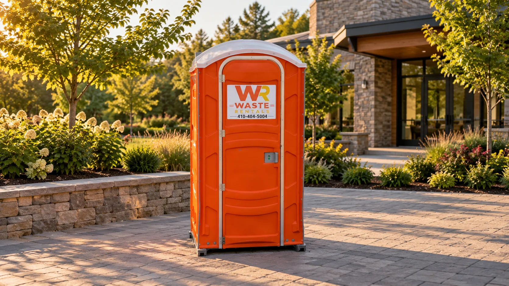 Orange Waste Rentals portable toilet beside a landscaped stone courtyard