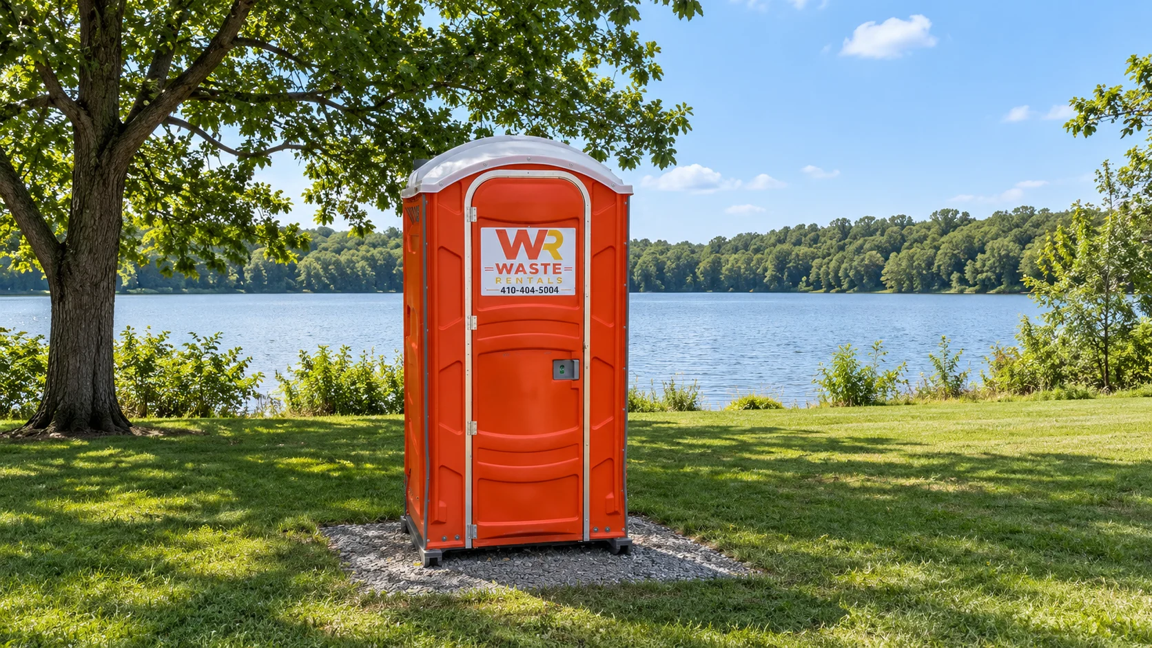 Orange Waste Rentals portable toilet beside a lakeside event lawn