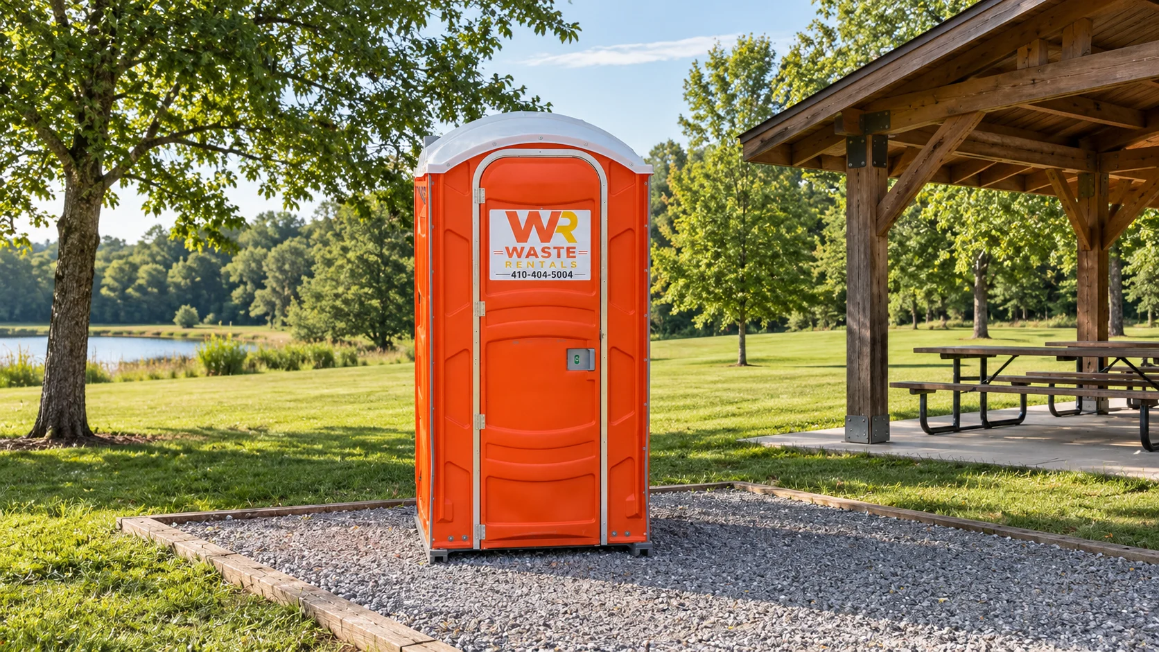 Orange Waste Rentals portable toilet beside a pavilion and open recreation field